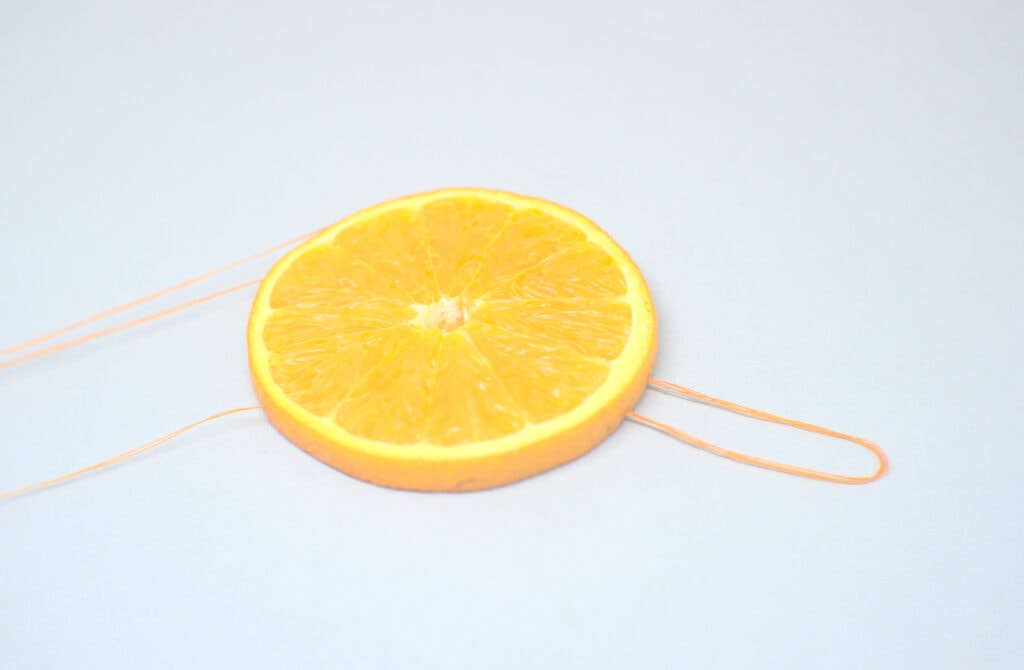 rodaja de una naranja con tiras y colgador hechos con hilo de coser