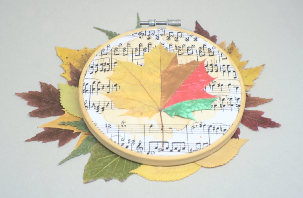 cuadro otoñal hecho con una hoja seca y un aro de bordado sobre un fondo de hojas