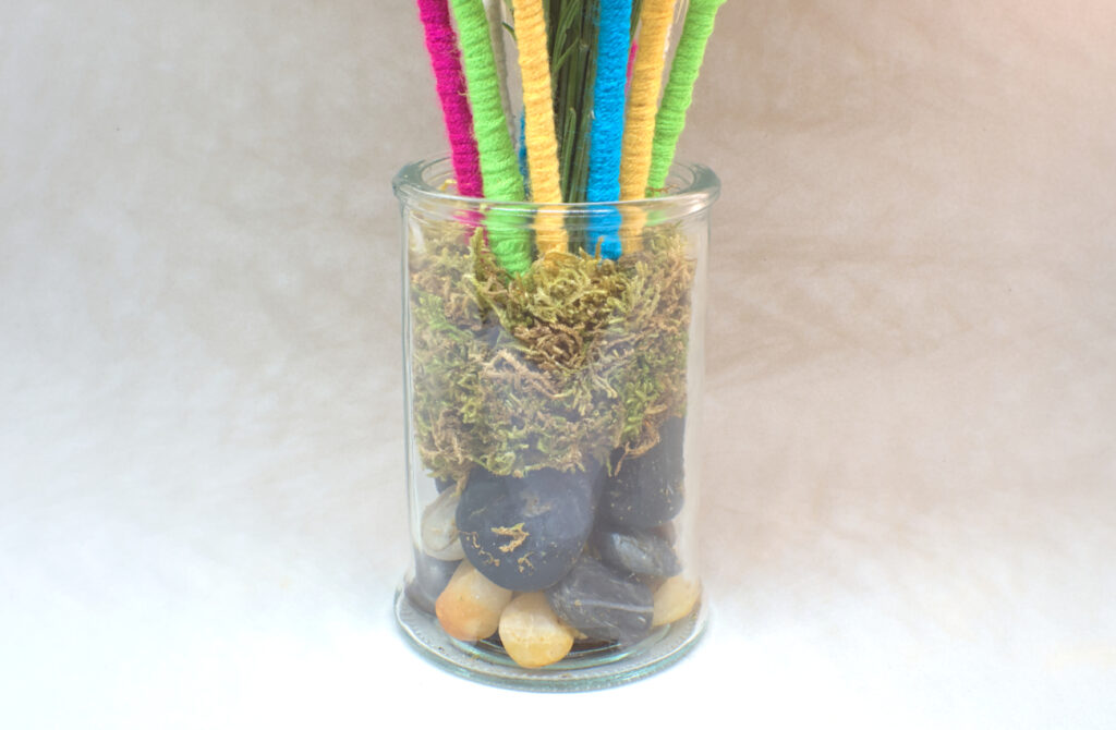 jarron de cristal con ramilletes de plantas silvestres decorados con lana de colores