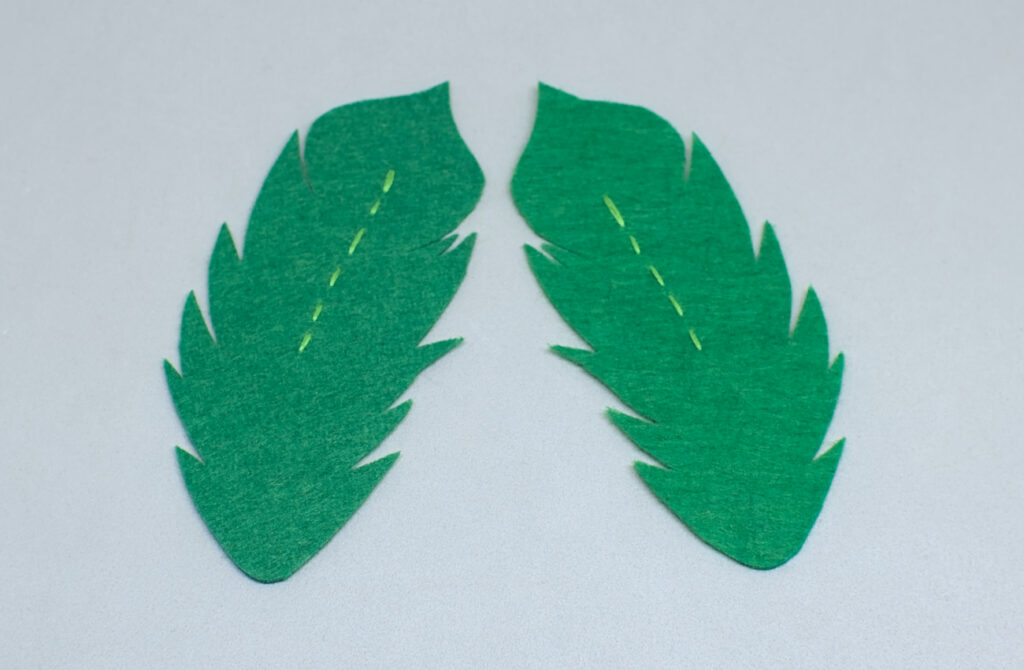 dos plumas de fieltro con puntadas de hilo verde