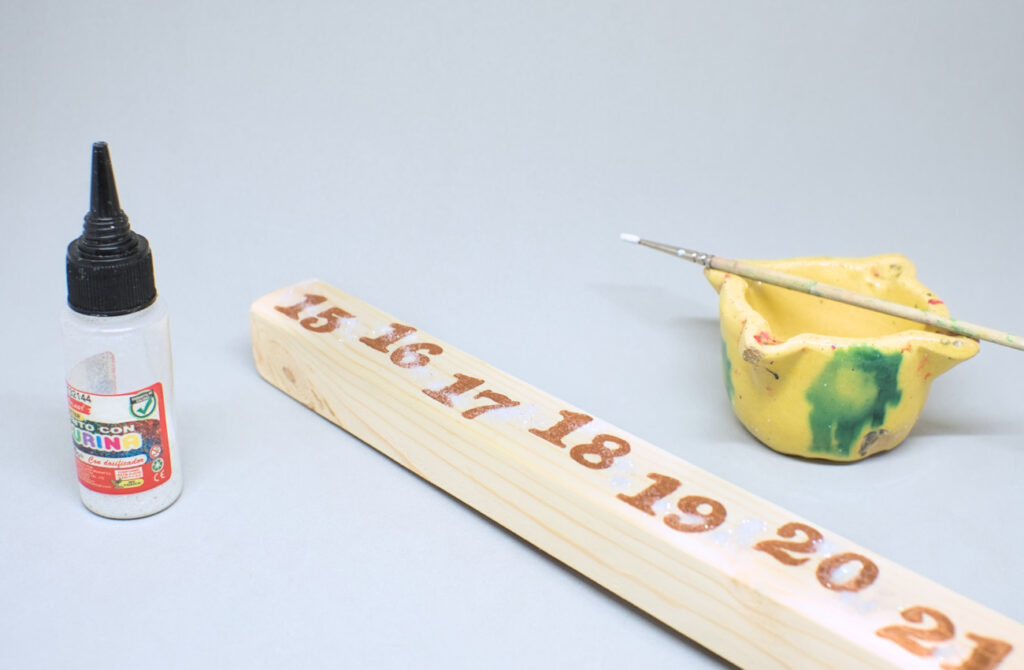 adhiriendo purpurina blanca en liston de madera con calendario