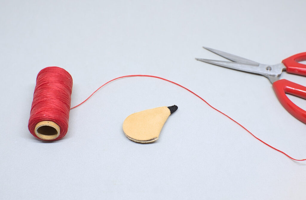 cortando hilo encerado rojo para ornamentar miniatura de bota de vino