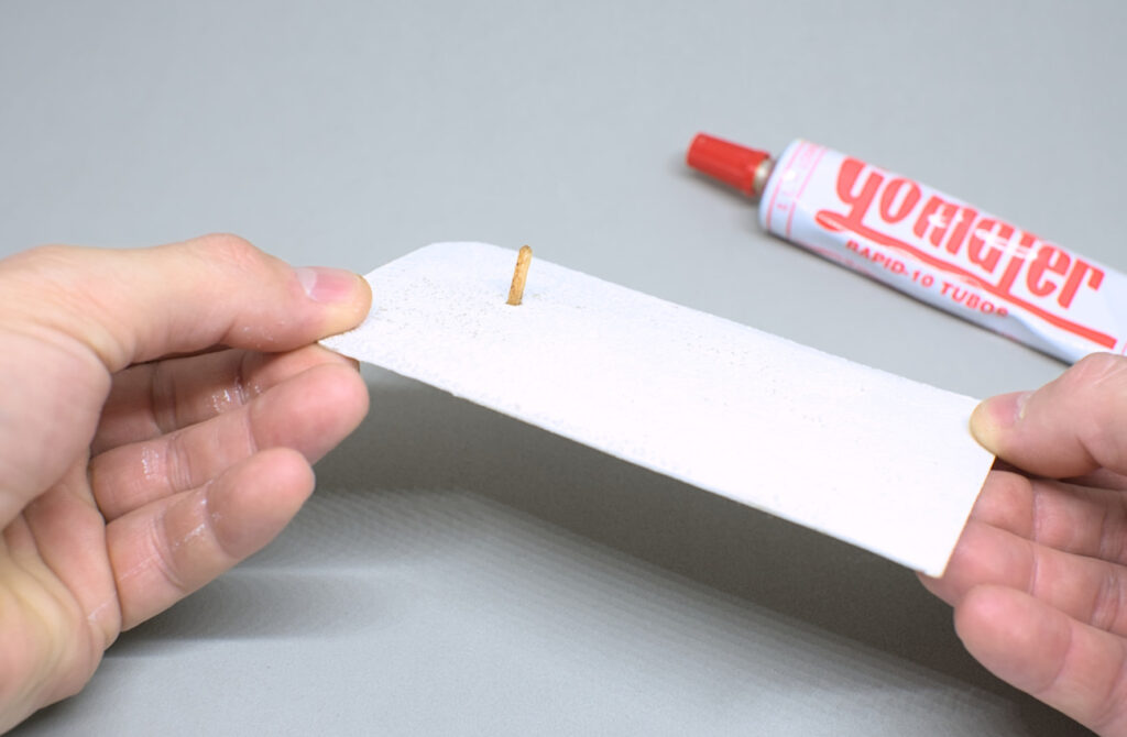 palito adherido en pieza de carton pintada en blanco