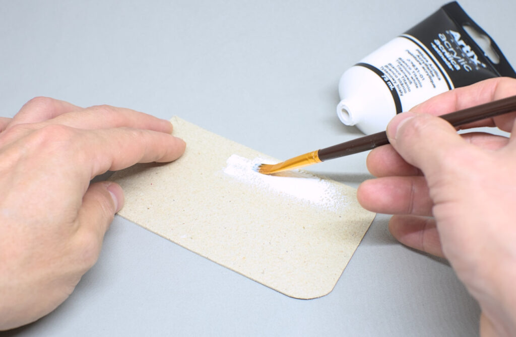pintando pieza rectangular de carton con pintura acrilica blanca