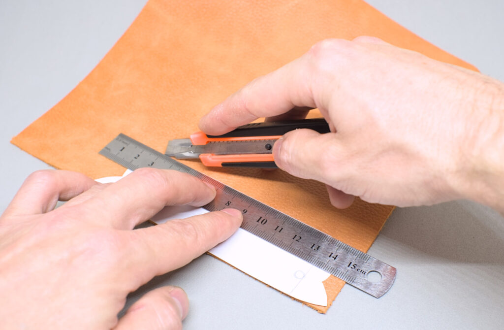 cortando pieza de cuero con cuter y patron de organizador de cables