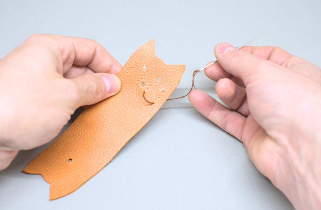 cosiendo bigotes de gato con hilo encerado en pieza de cuero