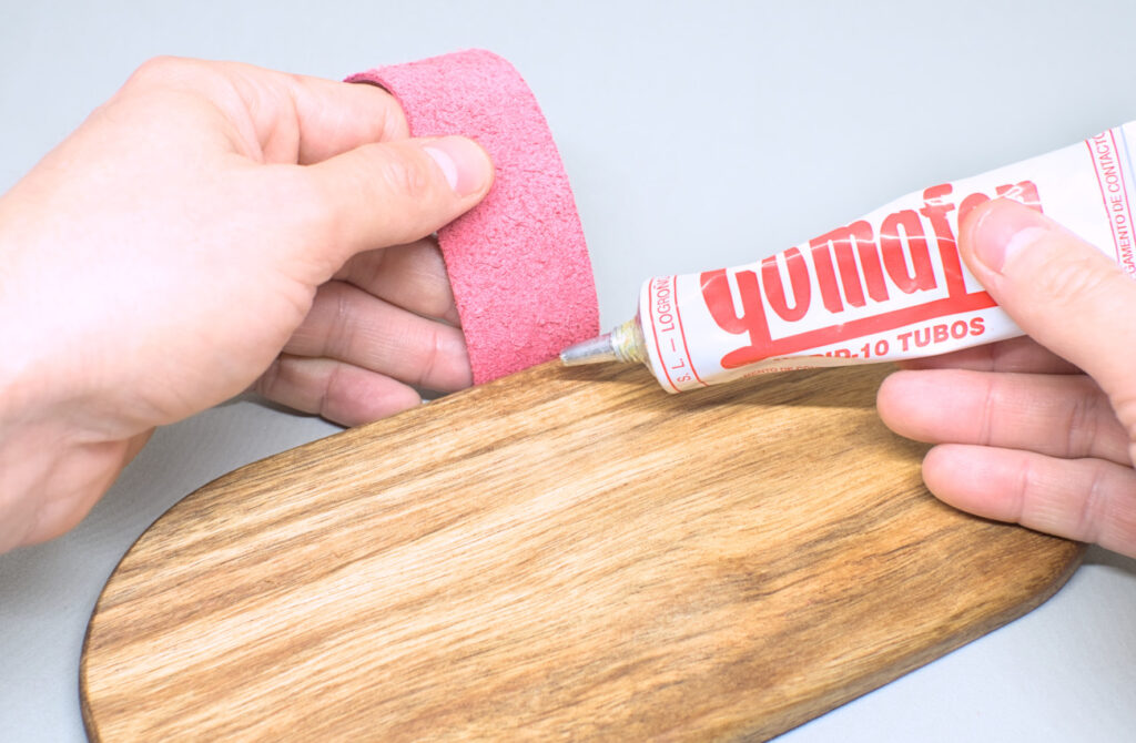 adhiriendo tira de cuero rosa con pegamento de contacto en lateral de bandeja de madera