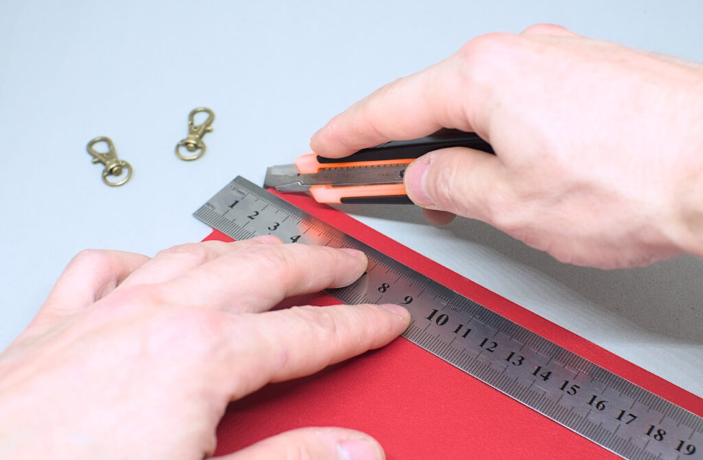 cortando tira de cuero rojo para hacer correa con mosquetones giratorios
