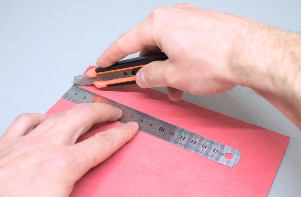 cortando tira de cuero rosa con cuter y regla