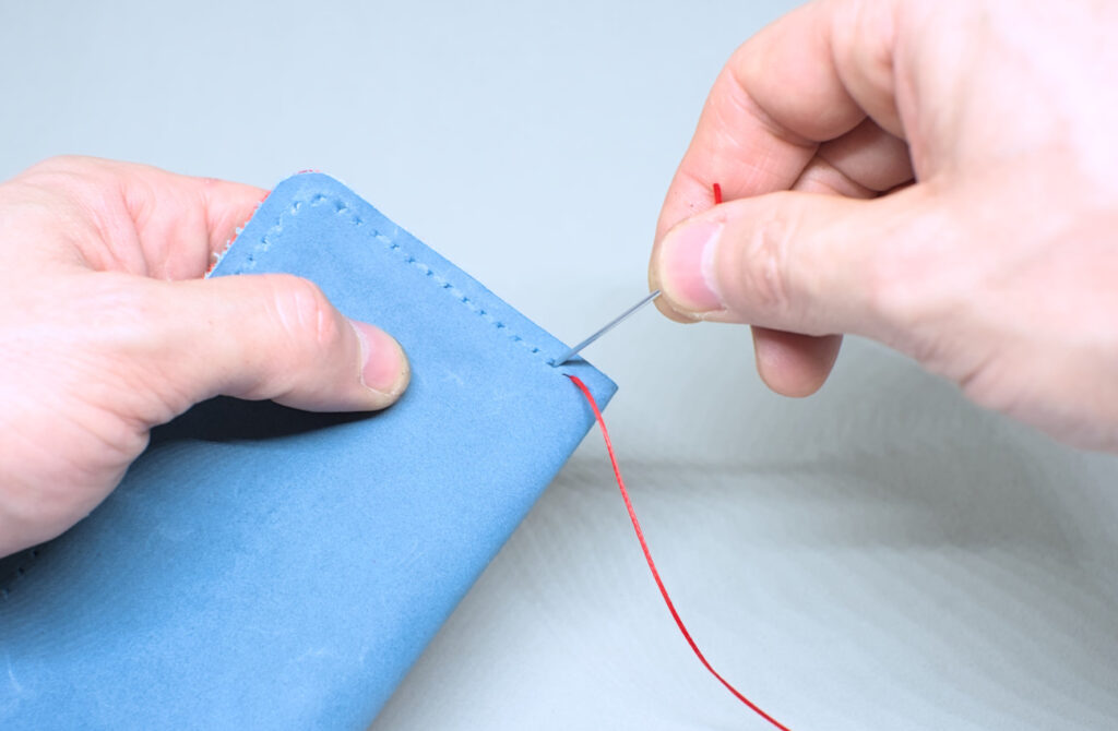 dando la tercera puntada con aguja e hilo encerado en anverso de estuche de cuero