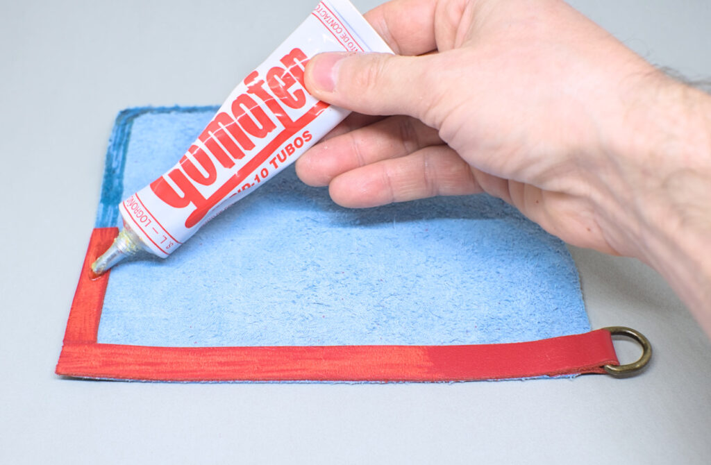 echando pegamento de contacto en tiras de cuero rojo adheridas en contorno de pieza para estuche