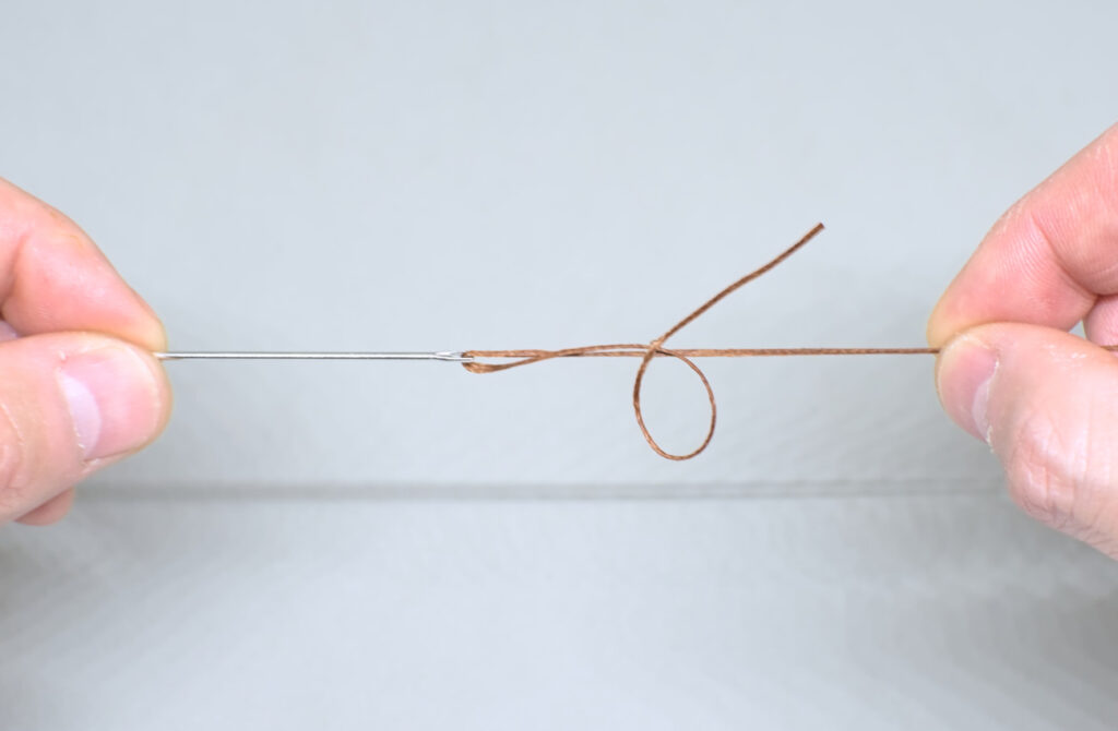 ajustando nudo de hilo encerado ensartado en aguja