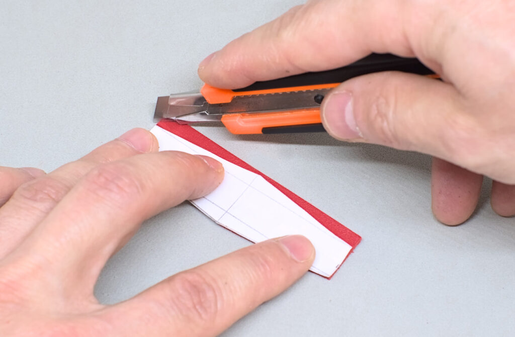 cortando pequeña tira de cuero rojo con forma de rombo