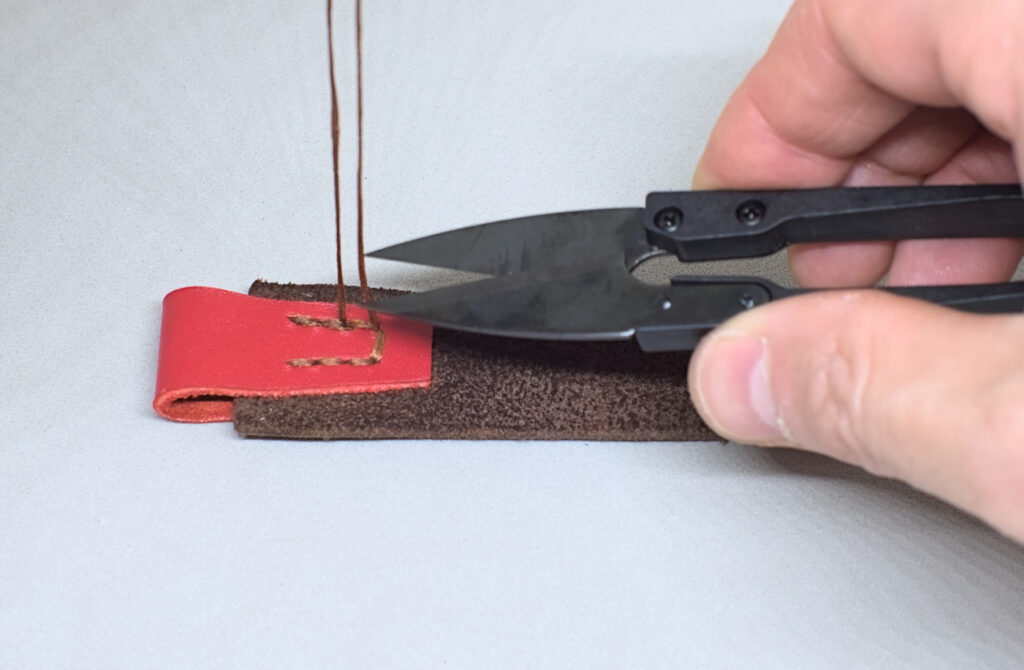 cortando sobrante de hilo encerado de costura de refuerzo para marcapaginas