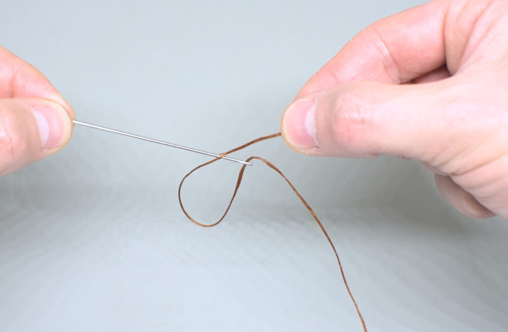 deslizando hacia abajo hilo encerado ensartado en aguja