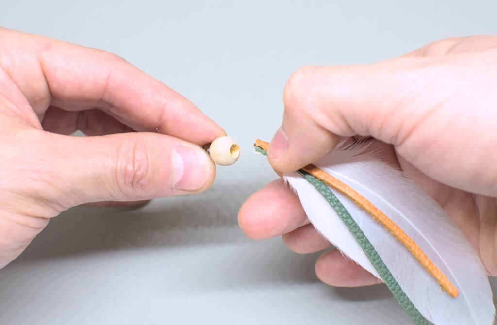 introduciendo en orificio los extremos de las tiras de cuero con pluma adherida