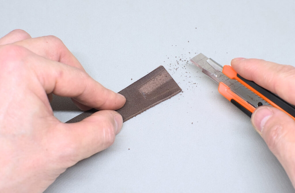 raspando superficie lisa de tira de cuero con cuter