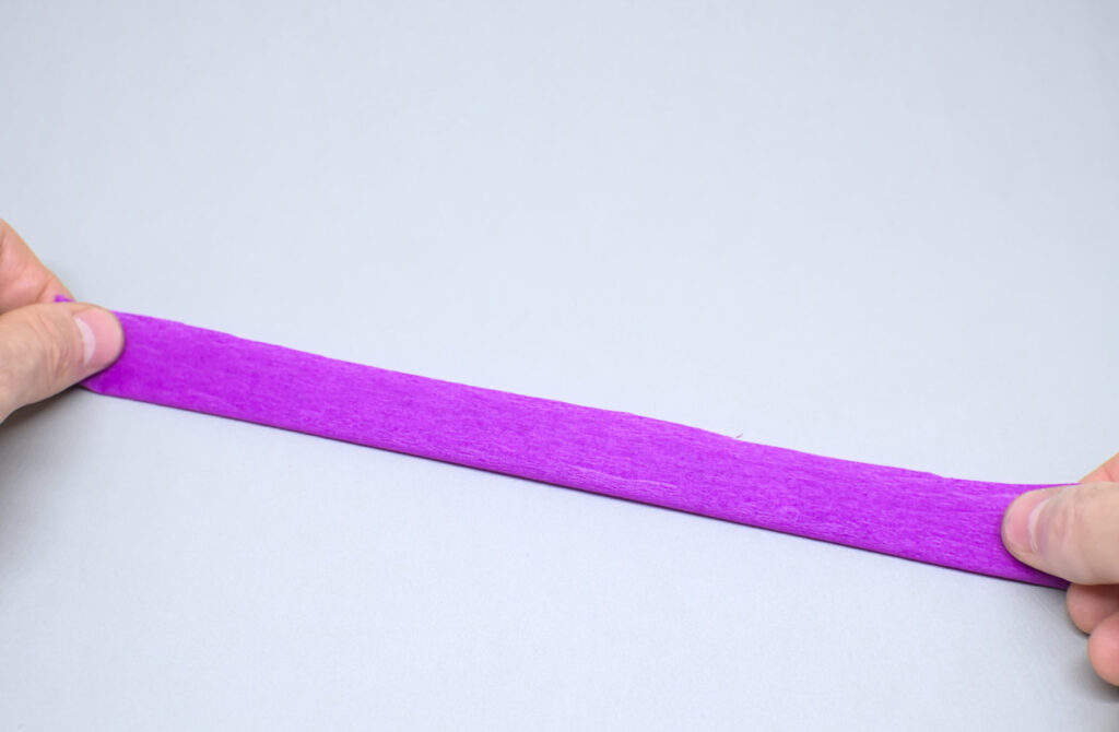 adhiriendo lados de tira doblada de papel crespon purpura