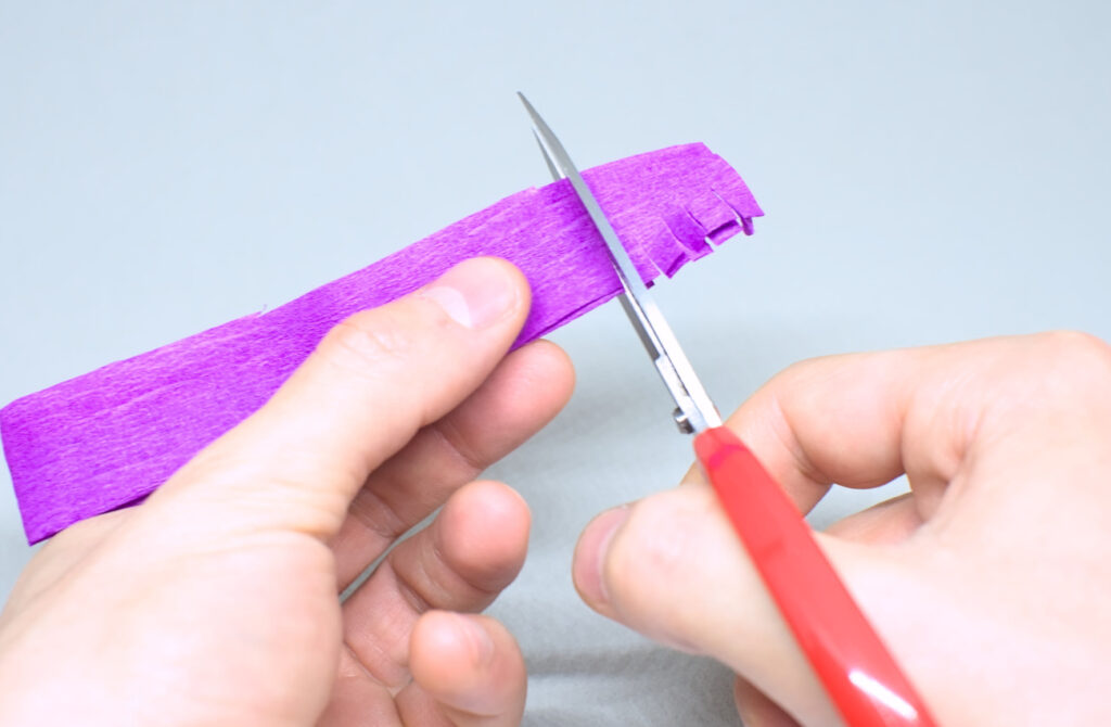 cortando flecos en tira doblada de papel crespon purpura