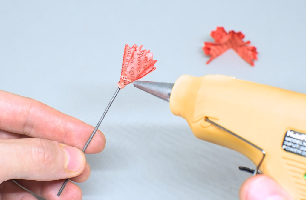 echando silicona caliente en contorno de primera pieza de papel para adherir segunda pieza doblada