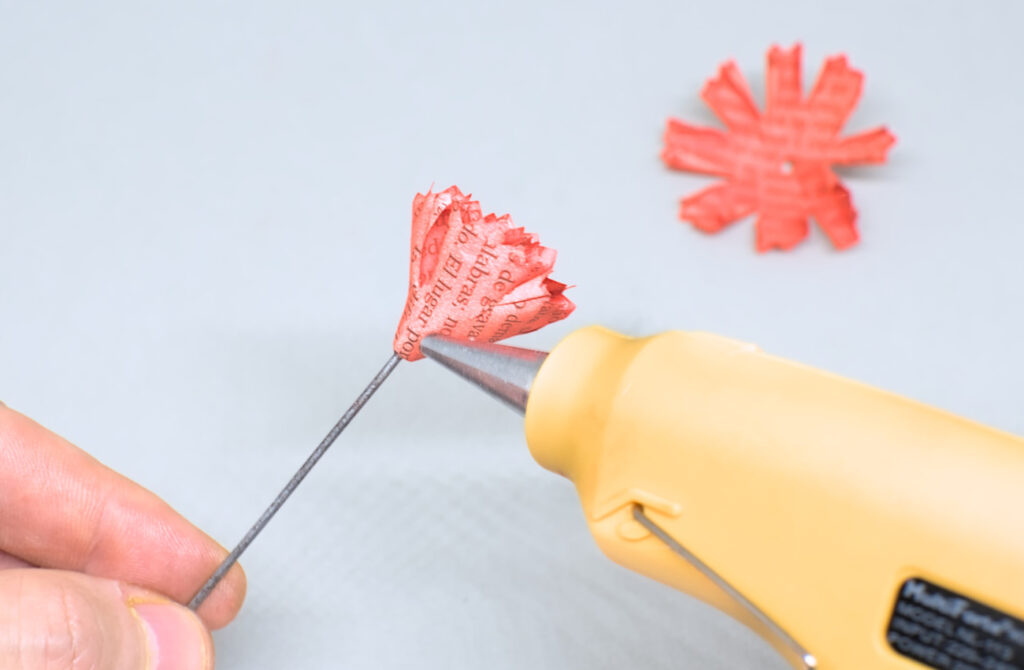 echando silicona caliente por el contorno de piezas de papel para adherir mas petalos de papel de clavel