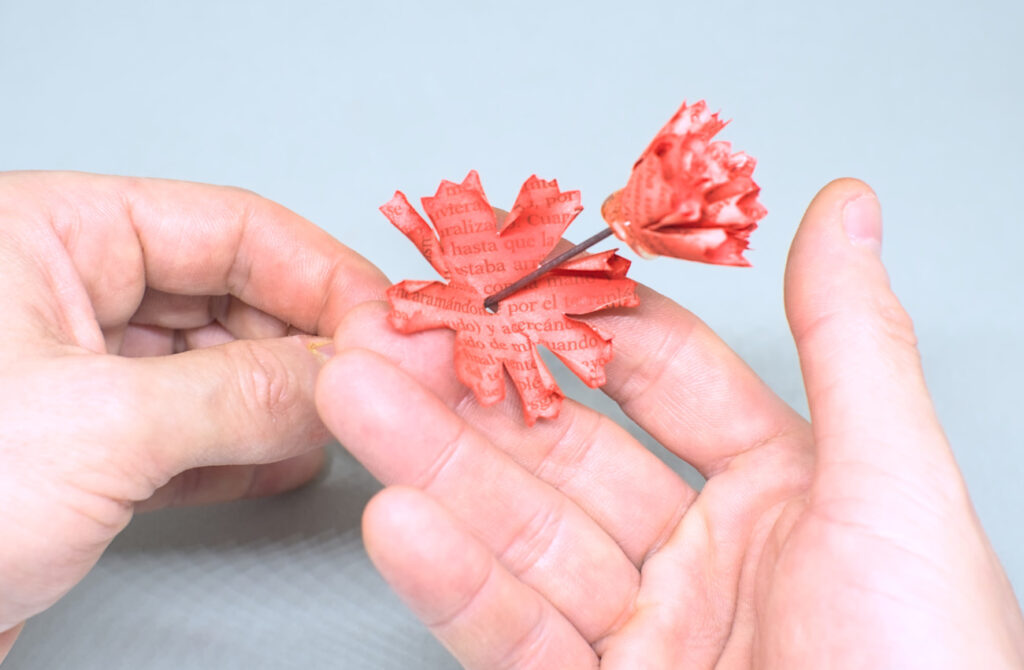 ensartando pieza de papel con orifico en alamabre para añadir mas petalos de clavel