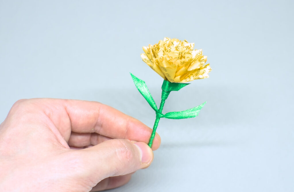 flor de clavel amarillo hecha con papel y cinta de raso verde