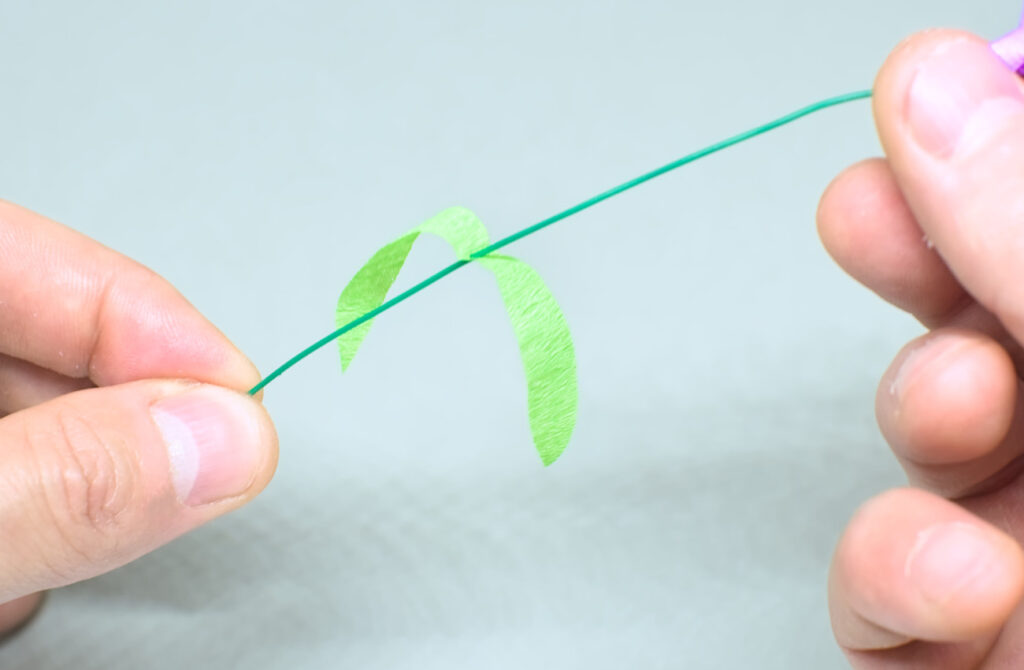 introduciendo alambre fino por corte en hojas simetricas de papel crespon verde