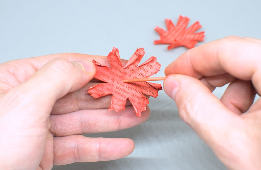 perforando con palillo el centro de hoja de papel con forma de petalos de clavel
