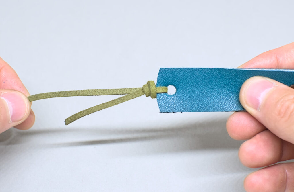 ajustando nudo corredizo para anudar tira de cuero para collar portagafas