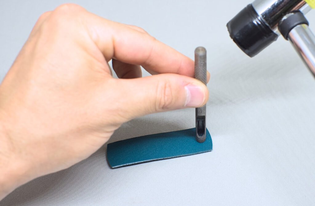 perforando orificios en tira de cuero verde con sacabocados