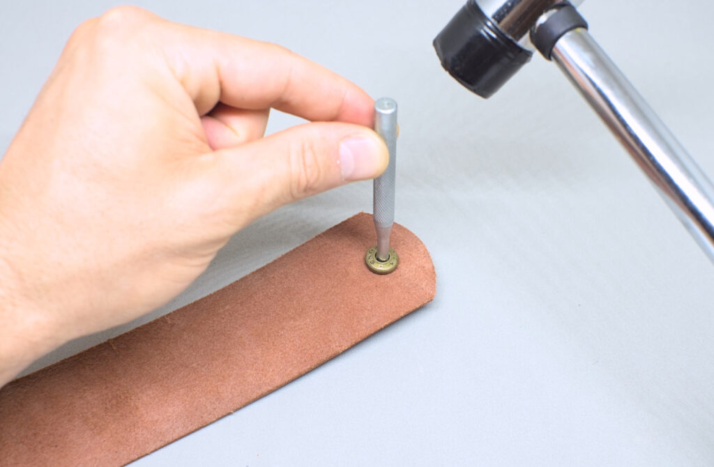 remachando pieza de boton a presion en funda de cuero para abanico